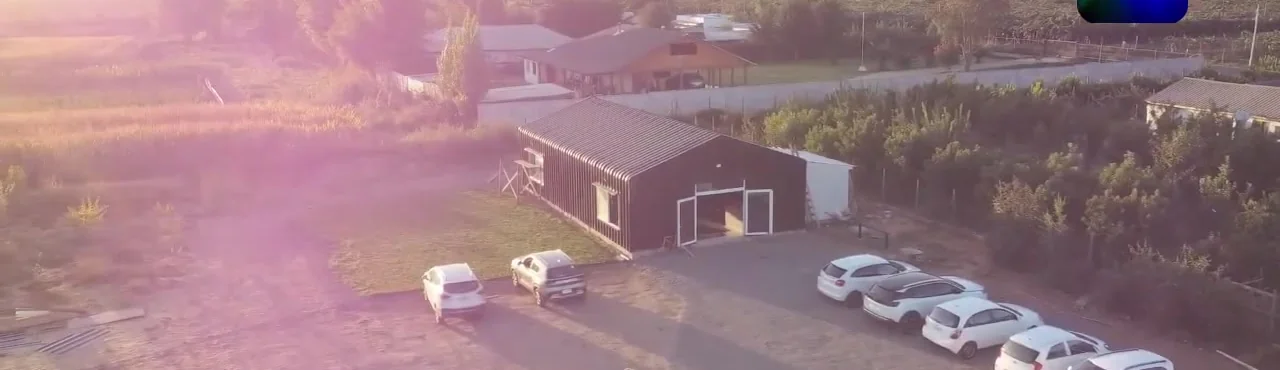 Galpón negro de Eleven Fit entre parcelas, autos estacionados y cerros de Cabaña Blanca al atardecer